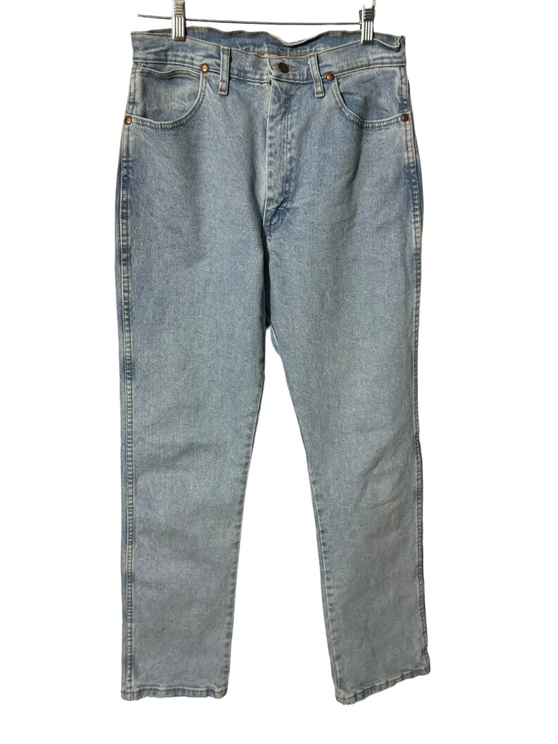 May include: Light blue denim jeans with a straight leg fit. The jeans have a classic five-pocket style and a button fly.