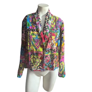 Puede incluir: Una chaqueta de manga larga con un vibrante patrón de patchwork multicolor con motivos de corazones, cuello tipo chal y cierre frontal de un solo botón. La prenda muestra una mezcla de colores rosa brillante, amarillo, azul y negro.