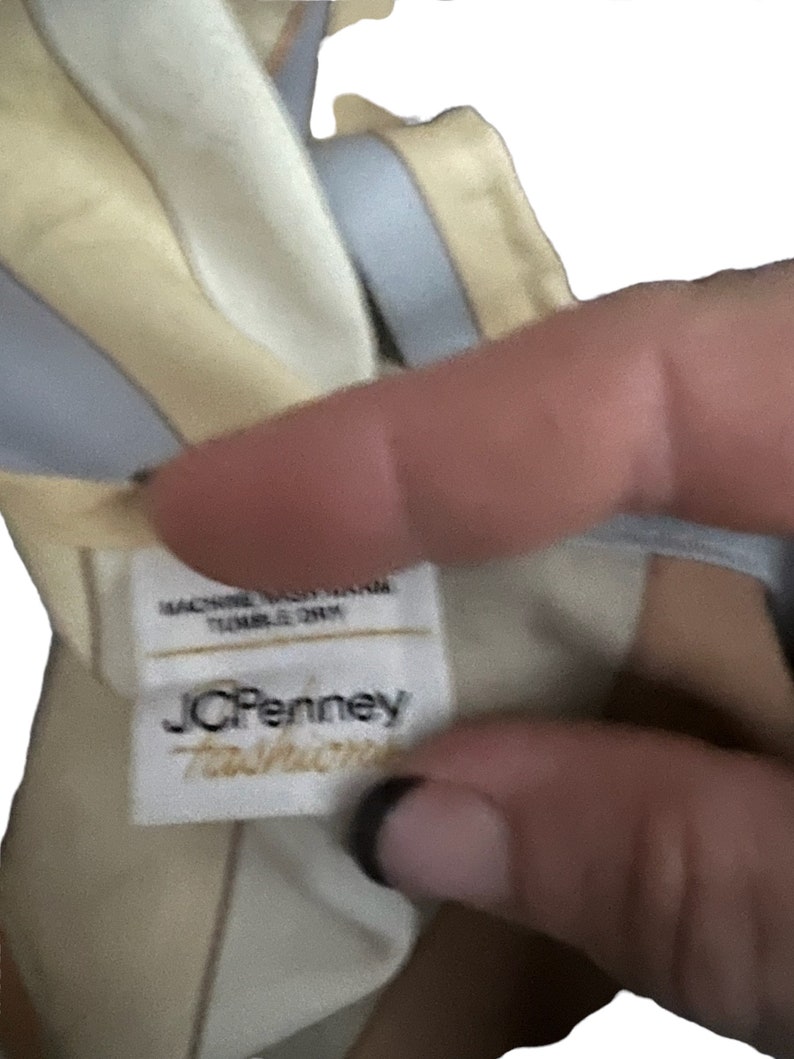 May include: A white tag with the text "JCPenney  Taffeta" in black lettering. The tag is attached to a yellow and blue striped fabric.