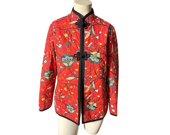 Puede incluir: Chaqueta acolchada roja con un estampado floral en verde azulado, amarillo y blanco. La chaqueta tiene cuello mandarín, ribete negro y cierres de rana. La chaqueta se exhibe en un maniquí.