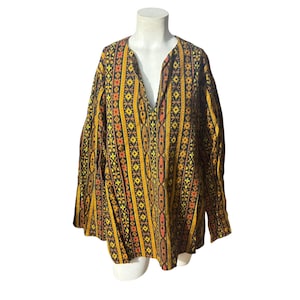May include: A long-sleeved tunic with a deep V-neck, displayed on a mannequin. The tunic features a repeating vertical pattern of orange, yellow, and black geometric shapes. The fabric appears to be a woven material.