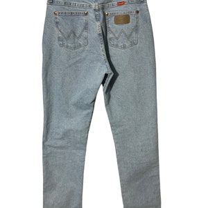 May include: A pair of light blue denim jeans with a brown leather patch on the back pocket that says "Wrangler".