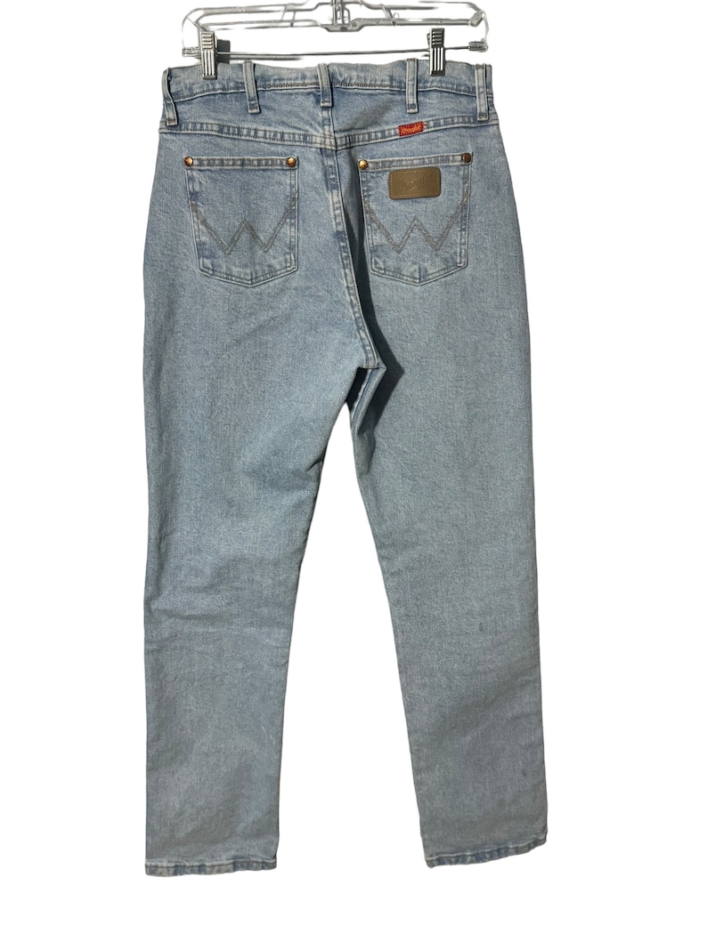 May include: A pair of light blue denim jeans with a brown leather patch on the back pocket that says "Wrangler".