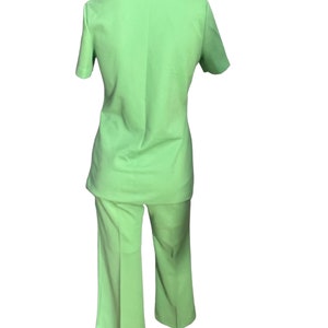 May include: A light green two-piece suit. The suit includes a short-sleeved collared shirt and matching flared pants. The outfit is displayed on a mannequin, showcasing the back of the garment.