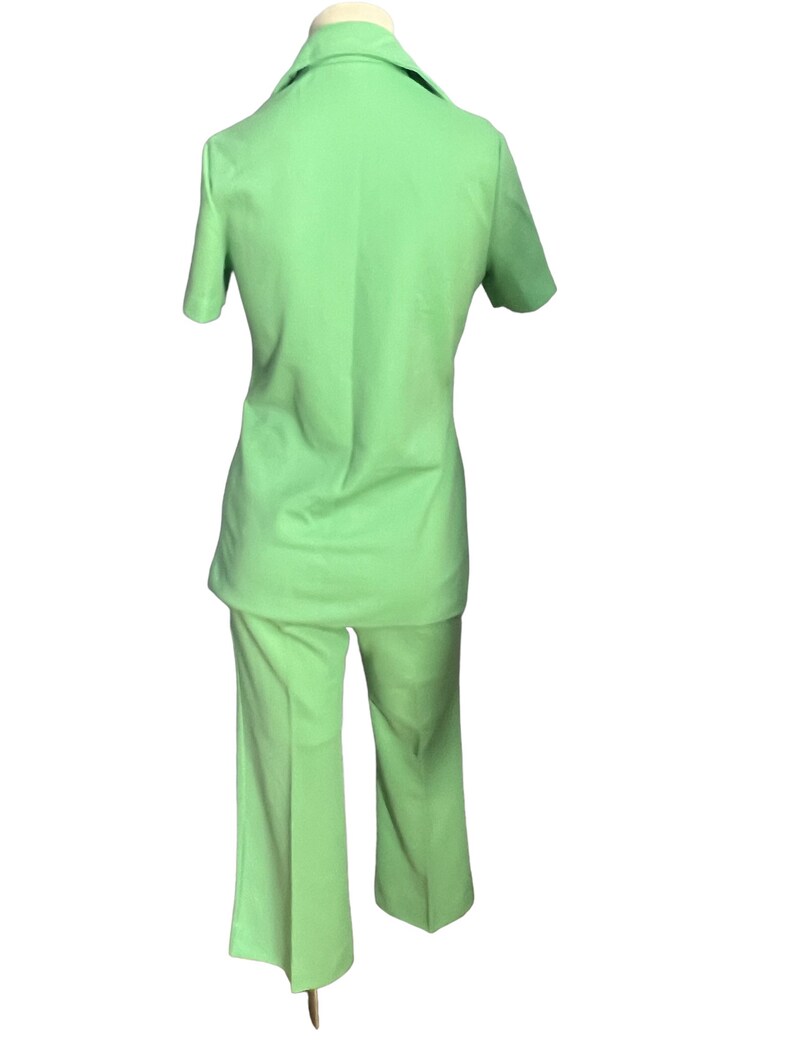 May include: A light green two-piece suit. The suit includes a short-sleeved collared shirt and matching flared pants. The outfit is displayed on a mannequin, showcasing the back of the garment.