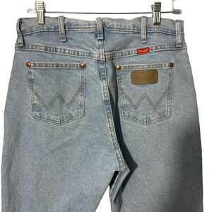 May include: Light blue denim jeans with a brown leather patch on the back pocket that says "Wrangler".