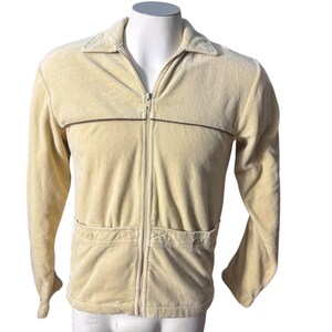 May include: A cream-colored velour jacket with a zipper closure and two pockets. The jacket has a brown stripe across the chest.