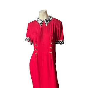 May include: A red dress with a black and white polka dot collar and sleeve cuffs. The dress has gold-coloured buttons down the front. The dress is displayed on a mannequin.