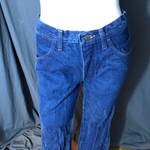 May include: Dark blue denim jeans with a classic five-pocket design. The jeans have a button and zipper closure, belt loops, and a straight leg fit. The fabric appears to be a medium-weight denim.
