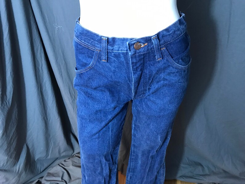 May include: Dark blue denim jeans with a classic five-pocket design. The jeans have a button and zipper closure, belt loops, and a straight leg fit. The fabric appears to be a medium-weight denim.