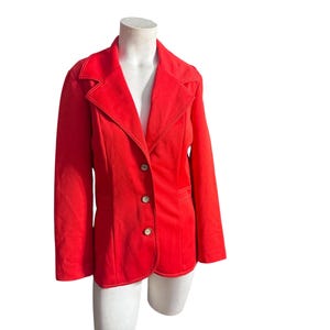 May include: A bright red blazer with a classic tailored design. The blazer features a notched lapel, three buttons, and visible stitching. The jacket is displayed on a white mannequin, showcasing its shape and style.
