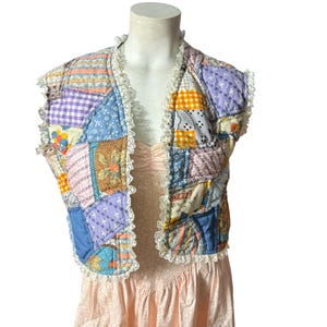 Könnte beinhalten: Eine Patchwork-Weste mit verschiedenen Farben und Mustern, darunter Blau, Rosa, Gelb und Grün. Die Weste hat einen Spitzenbesatz und ist ärmellos.