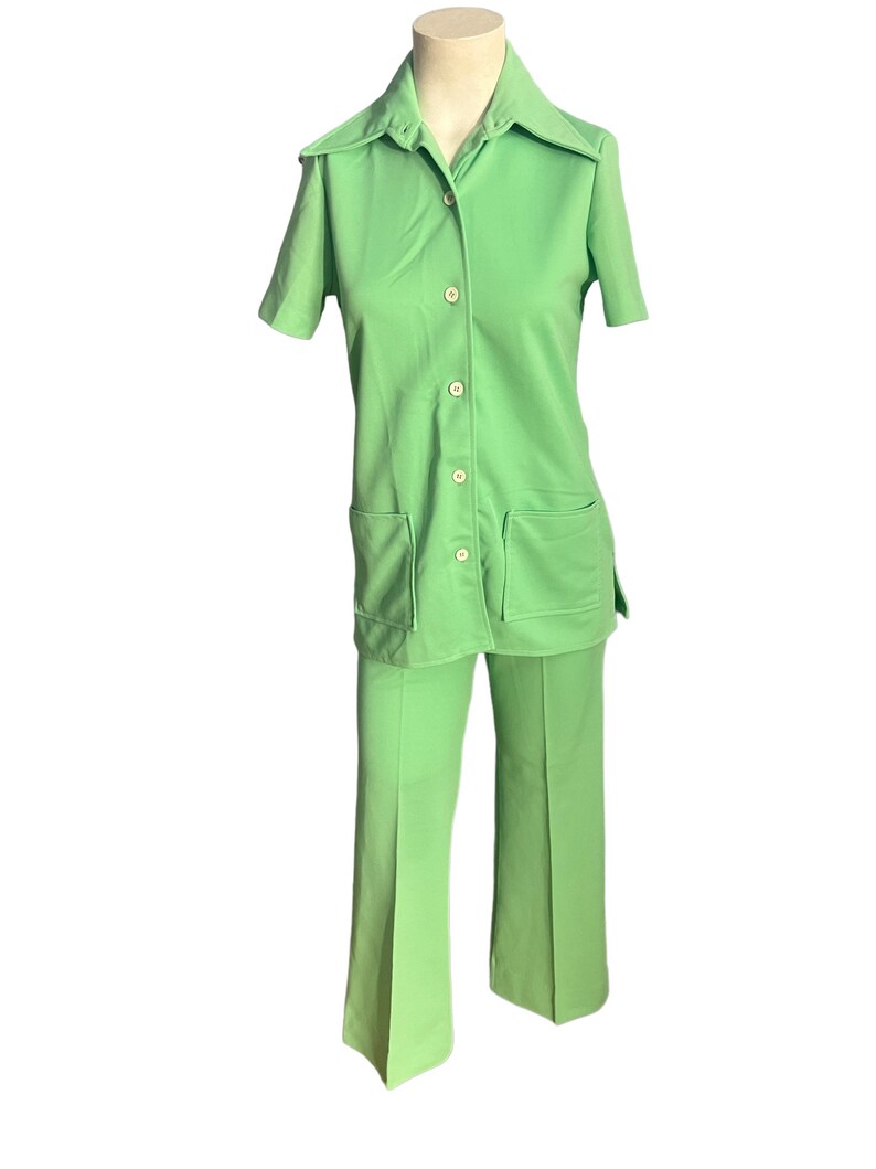 May include: A vintage lime green two-piece pantsuit. The short-sleeved collared shirt has two front pockets and button closures. The matching pants are flared. The outfit is displayed on a mannequin.