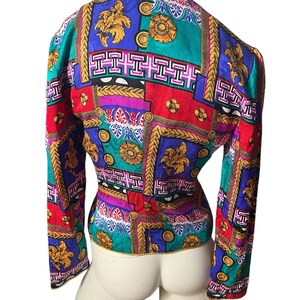 May include: A long-sleeved, fitted blouse with a colourful geometric pattern. The pattern features gold, red, blue, green, and pink colours. The blouse has a V-neck and long sleeves.
