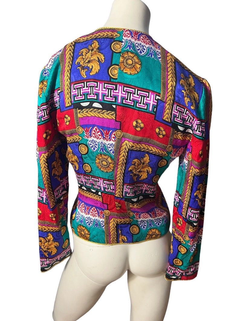 May include: A long-sleeved, fitted blouse with a colourful geometric pattern. The pattern features gold, red, blue, green, and pink colours. The blouse has a V-neck and long sleeves.