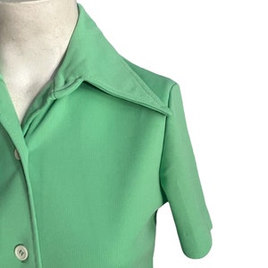 May include: A light green short-sleeved shirt with a pointed collar and two white buttons. The shirt is made of a smooth fabric and has a classic design. The shirt is displayed on a mannequin.