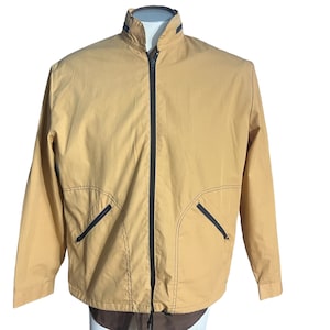 Puede incluir: Una chaqueta de cremallera de color beige con ribetes negros y dos bolsillos con cremallera en la parte delantera.