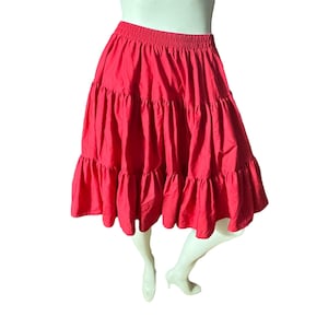 May include: A red tiered skirt with a ruffled hem. The skirt is made of a soft, flowing fabric and has an elastic waistband.
