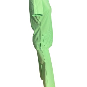 May include: A light green two-piece outfit. The top is a short-sleeved collared shirt with two front pockets and button closures. The matching pants are wide-legged. The outfit is made of a smooth, solid-colored fabric.