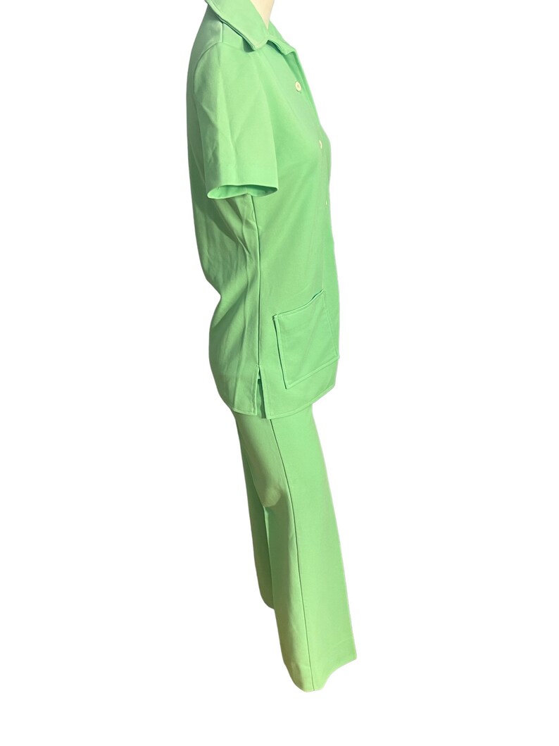 May include: A light green two-piece outfit. The top is a short-sleeved collared shirt with two front pockets and button closures. The matching pants are wide-legged. The outfit is made of a smooth, solid-colored fabric.