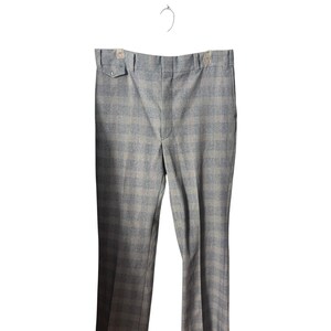 May include: Light gray plaid trousers hanging on a hanger. The pants have a classic plaid pattern in shades of gray and blue. The trousers have a button and a small pocket on the front.