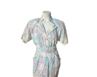 May include: A vintage dress with a pastel floral pattern in shades of pink, blue, and green. The dress features short sleeves, a collared neckline, and a belted waist. The dress has a button-down front and two front pockets.