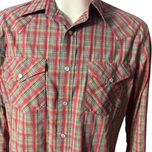 Op de afbeelding: Een rood, zwart en geel geruit overhemd met twee borstzakken en drukknoopsluitingen. Het overhemd heeft een klassieke westernstijl met een puntkraag en lange mouwen. De stof heeft een subtiele glans.