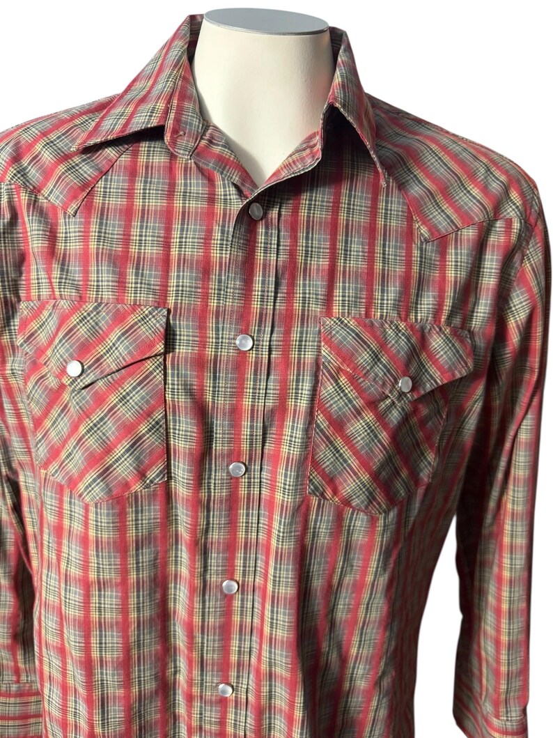 Op de afbeelding: Een rood, zwart en geel geruit overhemd met twee borstzakken en drukknoopsluitingen. Het overhemd heeft een klassieke westernstijl met een puntkraag en lange mouwen. De stof heeft een subtiele glans.