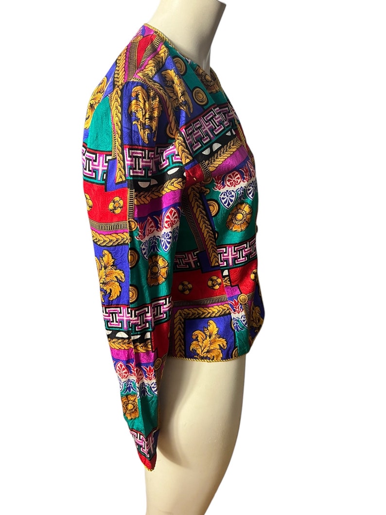 May include: A colourful, patterned jacket with a geometric design featuring gold accents. The jacket has long sleeves and a cropped length.