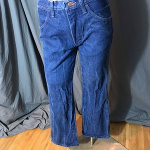 May include: Dark blue denim jeans with a classic five-pocket design. The jeans have a button and zipper closure, and a slight flare at the bottom of the legs. The jeans are displayed on a mannequin.