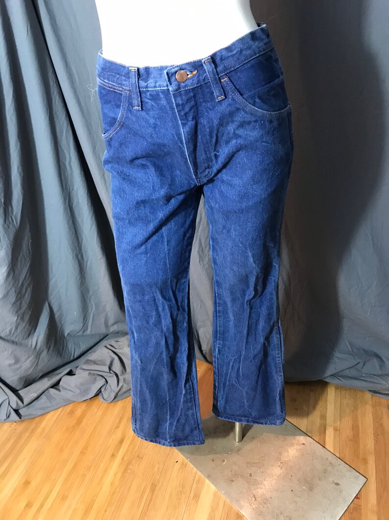 May include: Dark blue denim jeans with a classic five-pocket design. The jeans have a button and zipper closure, and a slight flare at the bottom of the legs. The jeans are displayed on a mannequin.