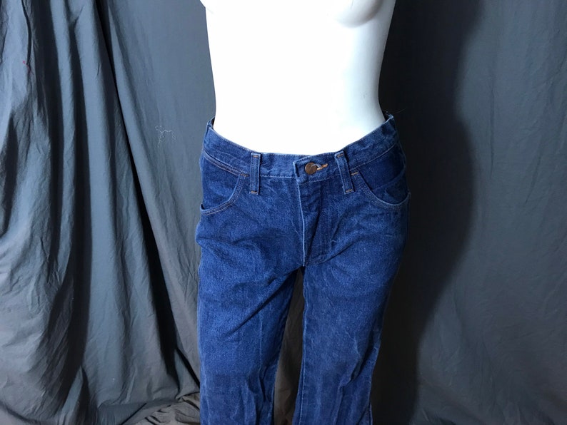 May include: Dark blue denim jeans with a classic five-pocket design. The jeans have a button and zipper closure, and a straight leg fit. The jeans are displayed on a mannequin.