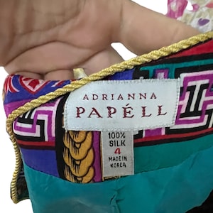 May include: A turquoise, purple, red and black silk dress with a gold rope trim. The dress has a label that reads "Adrianna Papell" and "100% Silk" with a size 4 and "Made in Korea".