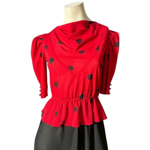 Peut inclure: Un chemisier à pois rouge et noir avec un ourlet à volants et un col plissé. Le chemisier a des manches 3/4 avec un détail de bouton à la manchette.