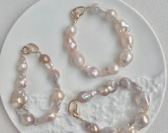 May include: Three bracelets made of irregular, lustrous baroque pearls in shades of soft pink, cream, and lavender. Each bracelet features a gold-toned metal clasp and a series of uniquely shaped, organic pearls strung together in a circular design.
