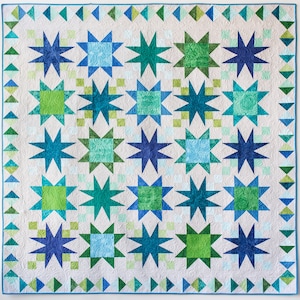 Könnte beinhalten: Eine Steppdecke mit weißem Hintergrund und einem sich wiederholenden Muster aus blauen und grünen Sternen. Die Sterne sind in einem Gittermuster angeordnet und von einem Rand aus blauen Dreiecken umgeben.