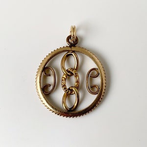 May include: A gold-toned pendant with a circular design featuring a repeating chain link pattern.