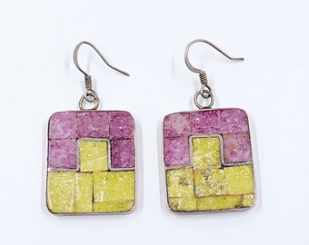 May include: A pair of silver earrings with square-shaped, geometric designs. The earrings are made of yellow and pink mosaic tiles.