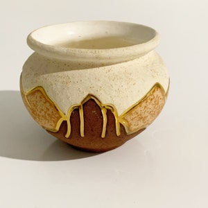 May include: A small, white ceramic planter with a brown and orange design. The planter has a textured surface and gold accents.
