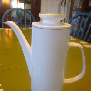 May include: White ceramic coffee pot with a green lid and green band around the bottom. The pot has a spout and a handle.