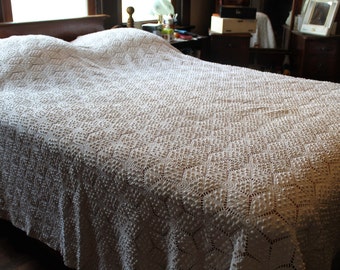 May include: A white crocheted bedspread with a raised diamond pattern. The bedspread is on a wooden bed frame.