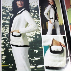 Könnte beinhalten: Ein weißer Strickcardigan mit schwarzem Besatz und Taschen. Der Cardigan wird an einem Model gezeigt, das eine weiße Hose trägt. Das Bild zeigt auch eine Nahaufnahme des Taschendetails.