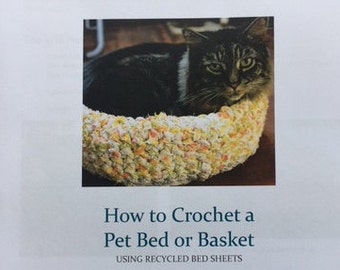 May include: A crocheted pet bed or basket made from recycled bed sheets. A tabby cat is resting inside the bed. The image includes the text "How to Crochet a Pet Bed or Basket Using Recycled Bed Sheets" and "Pamela Murphy 10/15/2006".