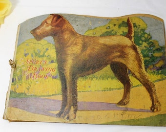 May include: Vintage children's drawing book with a brown and white dog on the cover. The cover is yellowed and has the text "Sport's Drawing Book" in red and black letters.