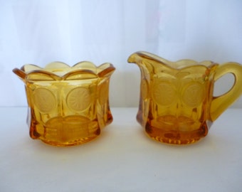 Azucarero y jarro de leche con tapa abierta de cristal con forma de moneda de color ámbar de FOSTORIA, con etiquetas