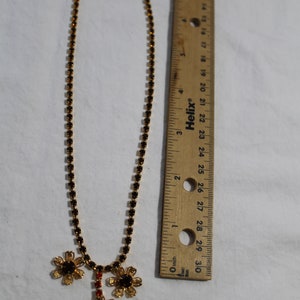 Puede incluir: Un collar de oro con una cadena de peque&ntilde;os diamantes de imitaci&oacute;n negros y un colgante de tres flores doradas con diamantes de imitaci&oacute;n negros. El collar mide 45,7 cm de largo.