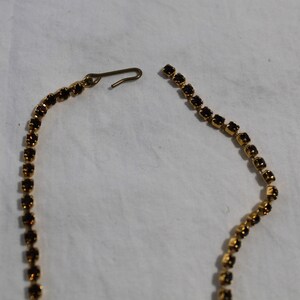 Puede incluir: Un collar de cadena dorada con un cierre roto. La cadena est&aacute; hecha de peque&ntilde;os diamantes de imitaci&oacute;n marrones oscuros.
