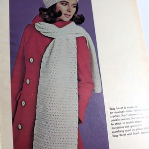 May include: A white crocheted beret and matching scarf. The beret has a simple design and the scarf is long and flowing. The model is wearing a red coat.