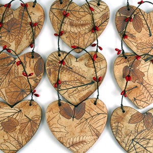 May include: A set of nine ceramic heart ornaments with a brown and white leaf pattern and red berries. The hearts are strung together with twine.