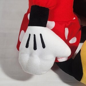 Pu&ograve; includere: Un peluche con una mano guantata bianca con linee nere, parte di un completo rosso a pois bianchi. Il giocattolo ha un polsino nero ed &egrave; visibile una scarpa gialla e nera.